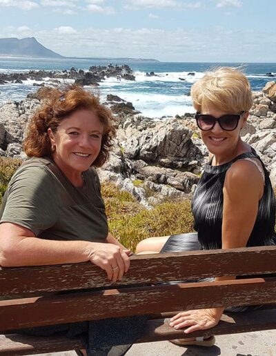 two women sitting on a bench at the seaside
