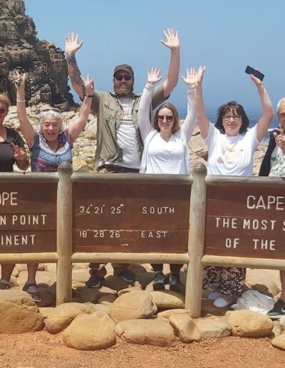 tour group standing behind a cape of good hope sign